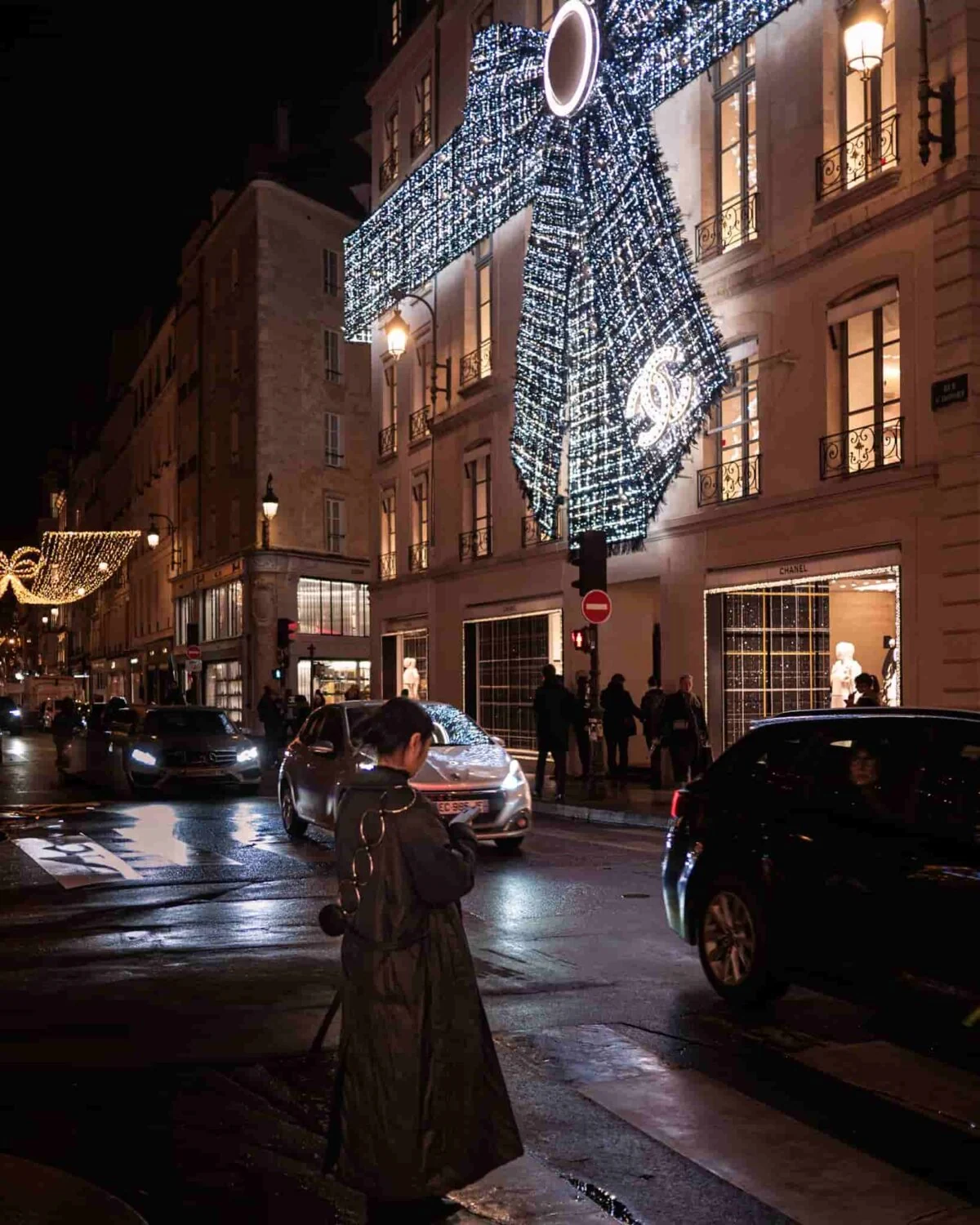 A girl standing in front of a Paris street. Buildings decorated with Christmas light in the background